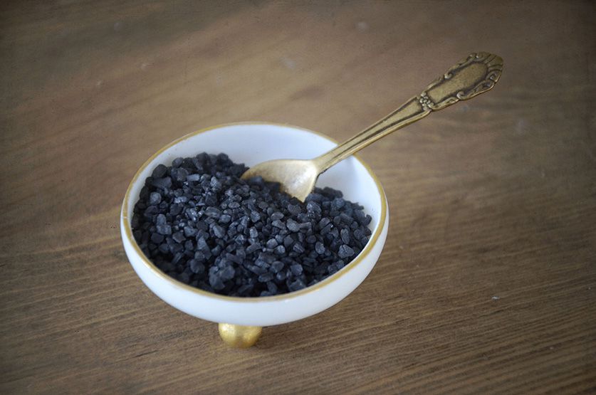 A bowl of black bath salt with a golden spoon